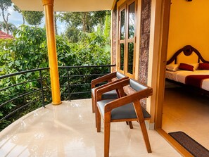 A balcony with a wooden bench, a bed with a red pillow, and a view of lush greenery.