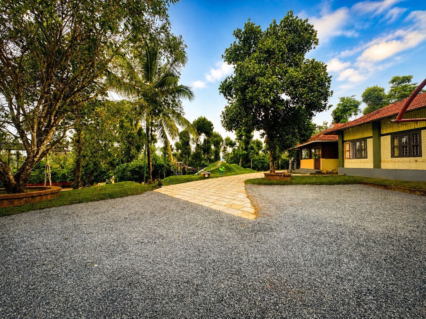 A paved driveway leading to a building with a red roof, surrounded by lush greenery and trees.