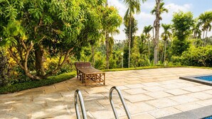 A swimming pool with metal handrails, a wooden bench, and lush greenery in the background.