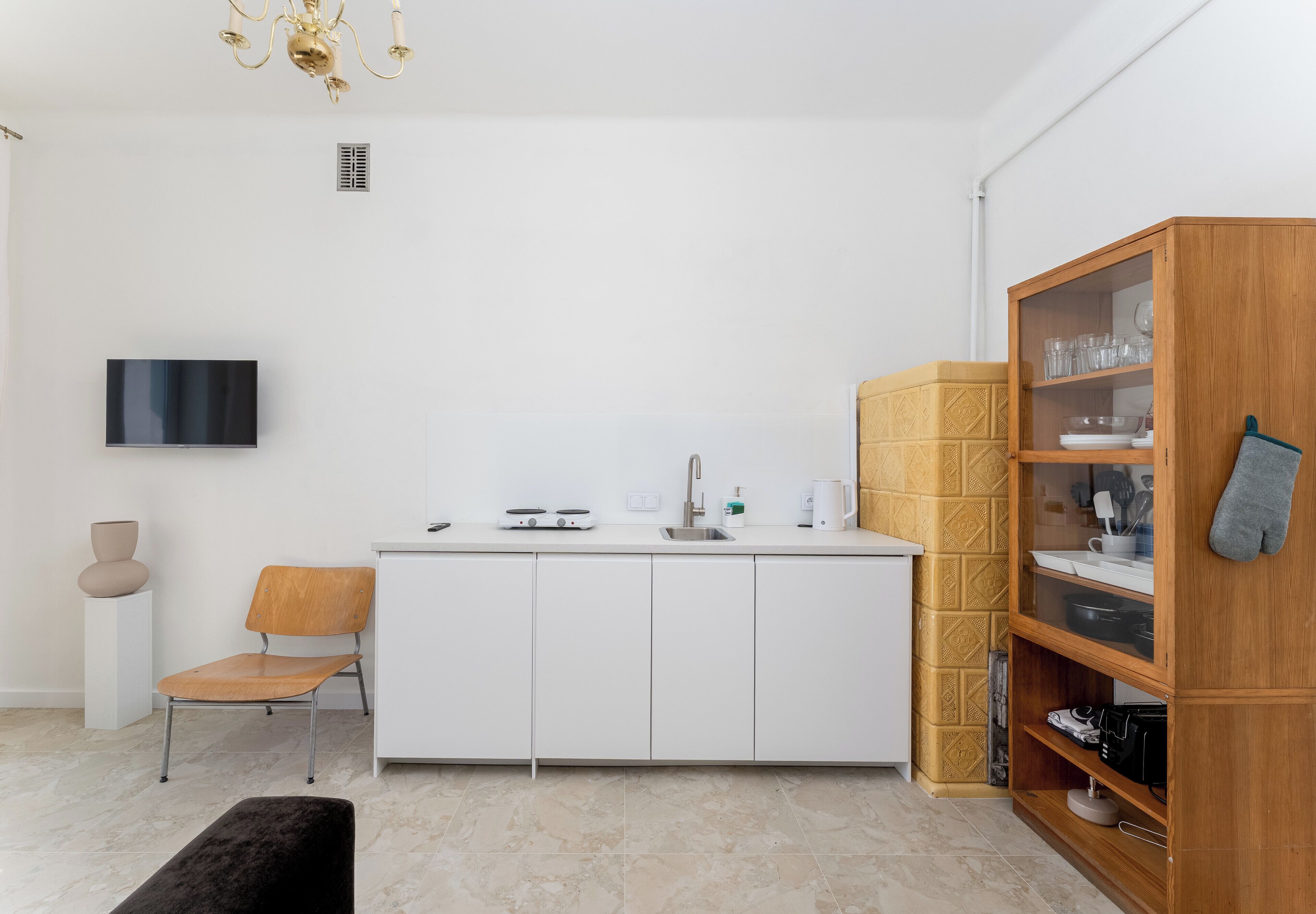 Eine moderne Küche mit weißen Schränken, einem eingebauten Herd, einer Spüle und einem Holzschrank mit Glastüren.