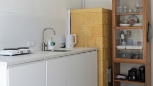 Keittiössä on valkoinen työtaso, kahvinkeitin, vedenkeitin ja lasiovilla varustettu kaappi, jossa säilytetään keittiötarvikkeita.