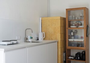 Eine Küche mit weißer Arbeitsplatte, einer Kaffeemaschine, einem Wasserkocher und einem Schrank mit Glastüren und Geschirr.