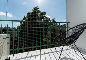 Ein Balkon mit grüner Metallreling, einem schwarzen Stuhl und einem Panasonic-Kühlschrank.