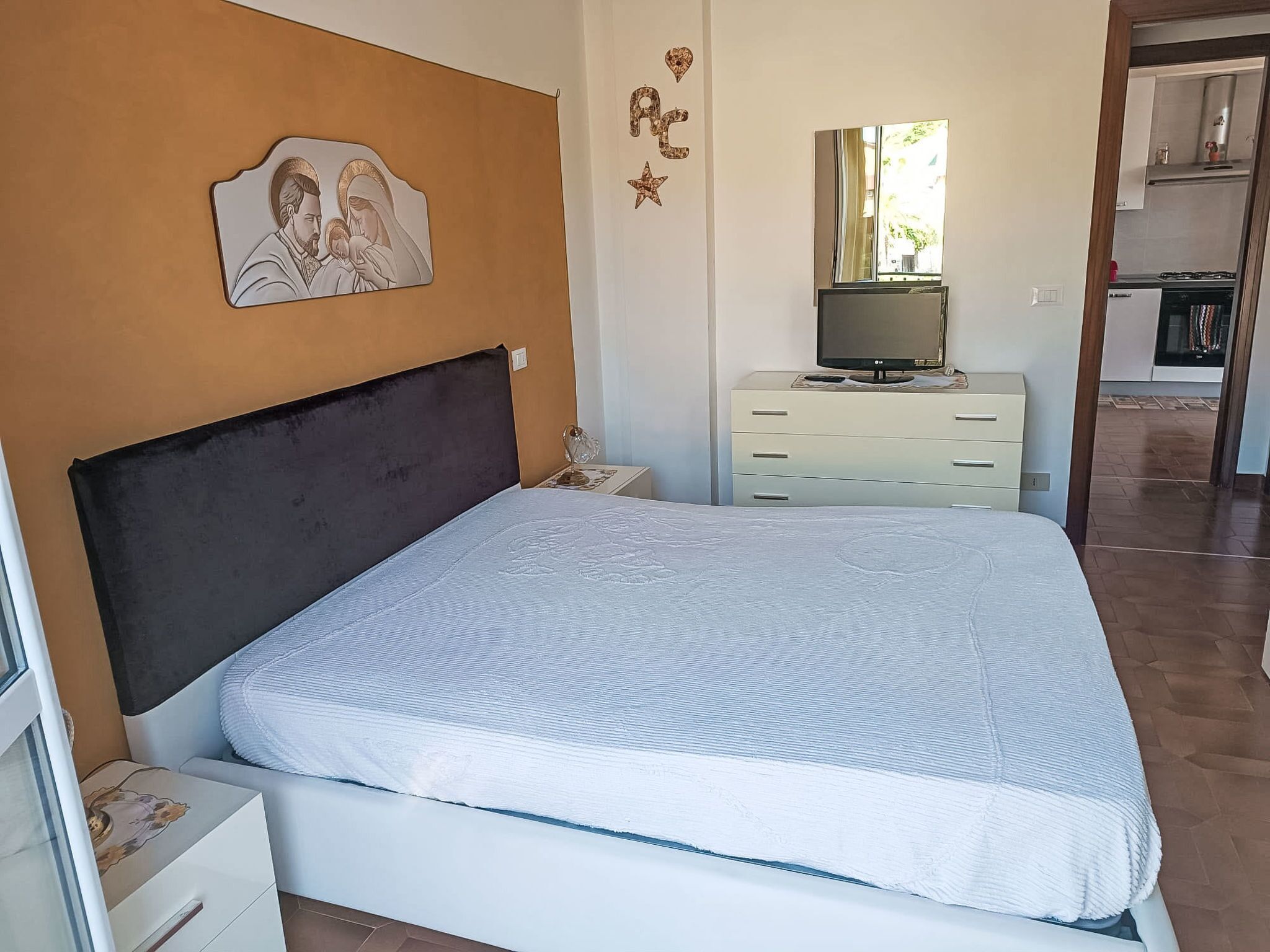 Ein Schlafzimmer mit einem Bett, einem Nachttisch, einer Kommode, einem Fernseher und einer Wanddekoration.
