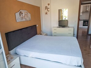Een slaapkamer met een bed, nachtkastje, kapstok, televisie en een decoratie aan de muur.