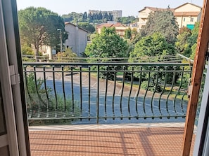 Blick von einem Balkon mit Metallgeländer auf einen Parkplatz und Gebäude im Hintergrund.