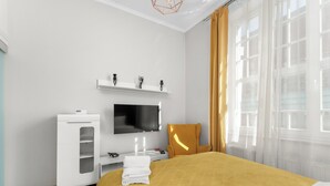 A hotel room with a bed, a television, a wardrobe, and a window with curtains. - Topolowa Comfort Apartment (Kraków)
