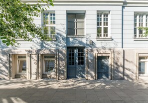 Ein Gebäude mit einem zentralen Eingang, mehreren Fenstern und einer Tür, über der ein Schild angebracht ist.