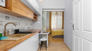 A compact kitchen with a wooden countertop, a sink, and a built-in stove. There is a small dining area with stools and a window with curtains. - Topolowa Comfort Apartment (Kraków)