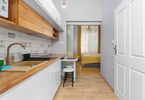 Eine kompakte Küche mit Holzarbeitsplatte, Spüle und integriertem Herd. Ein kleiner Essbereich mit Hockstühlen und ein Fenster mit Vorhängen.