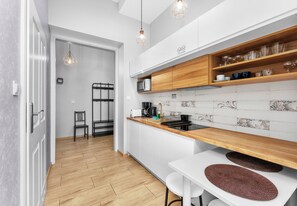 Une cuisine moderne avec des armoires blanches, des comptoirs en bois et un four à micro-ondes. On y trouve deux lampes suspendues, une chaise et une table à manger avec des sets de table.