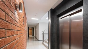 A hallway with a brick wall, a metal elevator, and a staircase with a metal railing. - Podgórze Boutique Studio (Kraków)
