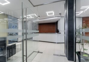 A modern reception area with glass partitions, a reception desk, a brick wall, and a potted plant. - Podgórze Boutique Studio (Kraków)