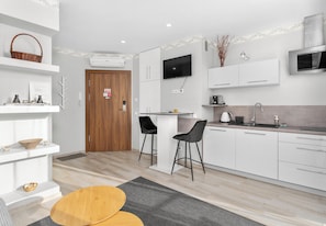 Une cuisine moderne avec des meubles blancs, une porte en bois, un téléviseur fixé au-dessus du comptoir et un four à micro-ondes.