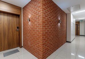 A hallway with a wooden door, a brick wall, and a tiled floor. - Podgórze Boutique Studio (Kraków)