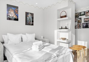 Une chambre d’hôtel avec un lit, des murs blancs, une étagère blanche et une petite table en bois.
