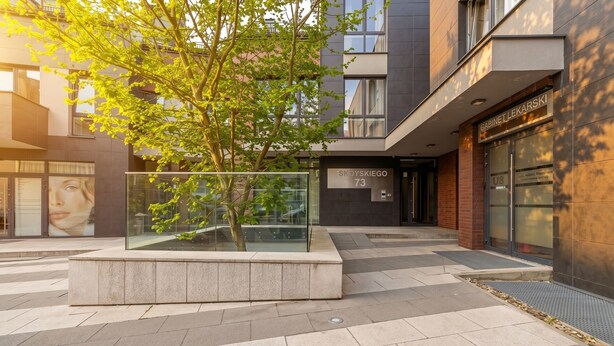 A modern building with a glass facade, a visible entrance, and a tree in a planter. - Podgórze Boutique Studio (Kraków)