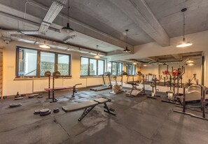 A gym with various exercise equipment, large windows, and a concrete ceiling. - Podgórze Boutique Studio (Kraków)