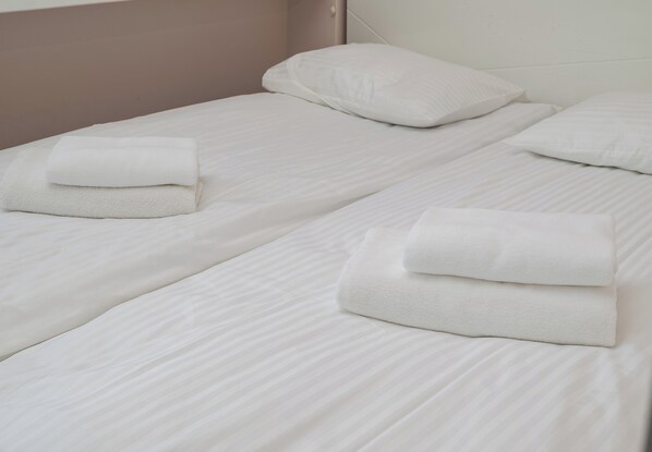 Ein Hotelzimmer mit zwei Einzelbetten, jedes mit einem ordentlich gefalteten weißen Handtuch.
