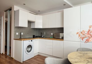 A compact kitchen with a washing machine, a microwave, and a dining area with a table. - Zgoda 13 Modern City Apartment (Warszawa)