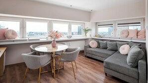 Uma sala de estar moderna com uma mesa redonda, sofás cinzentos e vista para a cidade através de grandes janelas.