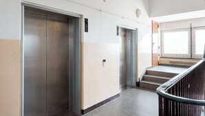 Corredor com dois elevadores e escadas que levam a um andar superior.