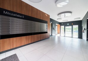 Un hall d’entrée moderne, doté d’une rangée de casiers numérotés, d’un mur décoratif en bois et d’une entrée avec une porte en verre.
