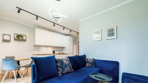 Ein modernes Wohnzimmer mit einem blauen Sofa, einem kleinen runden Tisch und einer Küche im Hintergrund.