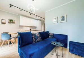 Ein modernes Wohnzimmer mit einem blauen Sofa, einem kleinen runden Tisch und einer Küche im Hintergrund.