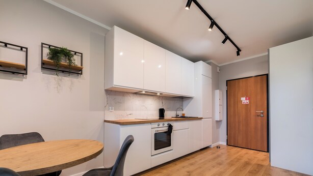 Eine moderne Küche mit weißen Schränken, einer Holz Arbeitsplatte und einem eingebauten Backofen. Ein Esstisch mit Stühlen und eine Pflanze an der Wand sind ebenfalls vorhanden.