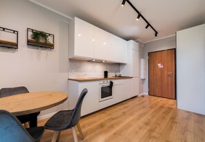 A modern kitchen with white cabinets, a wooden countertop, and a built-in oven. There is a dining table with chairs and a plant on the wall. - Posnania Comfort Studio with Garden (Poznań)