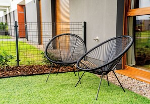 Two black wire-framed chairs placed on a well-maintained lawn with a metal fence and a building in the background. - Posnania Comfort Studio with Garden (Poznań)
