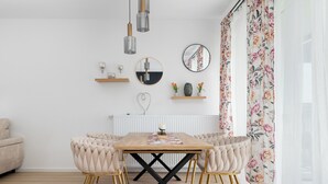 A dining area with a wooden table, upholstered chairs, and a black X-shaped base. - Zielonego Mostu Cozy Elegant Apartment (Szczecin)