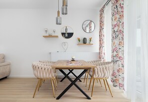 A dining area with a wooden table, upholstered chairs, and a black X-shaped base. - Zielonego Mostu Cozy Elegant Apartment (Szczecin)