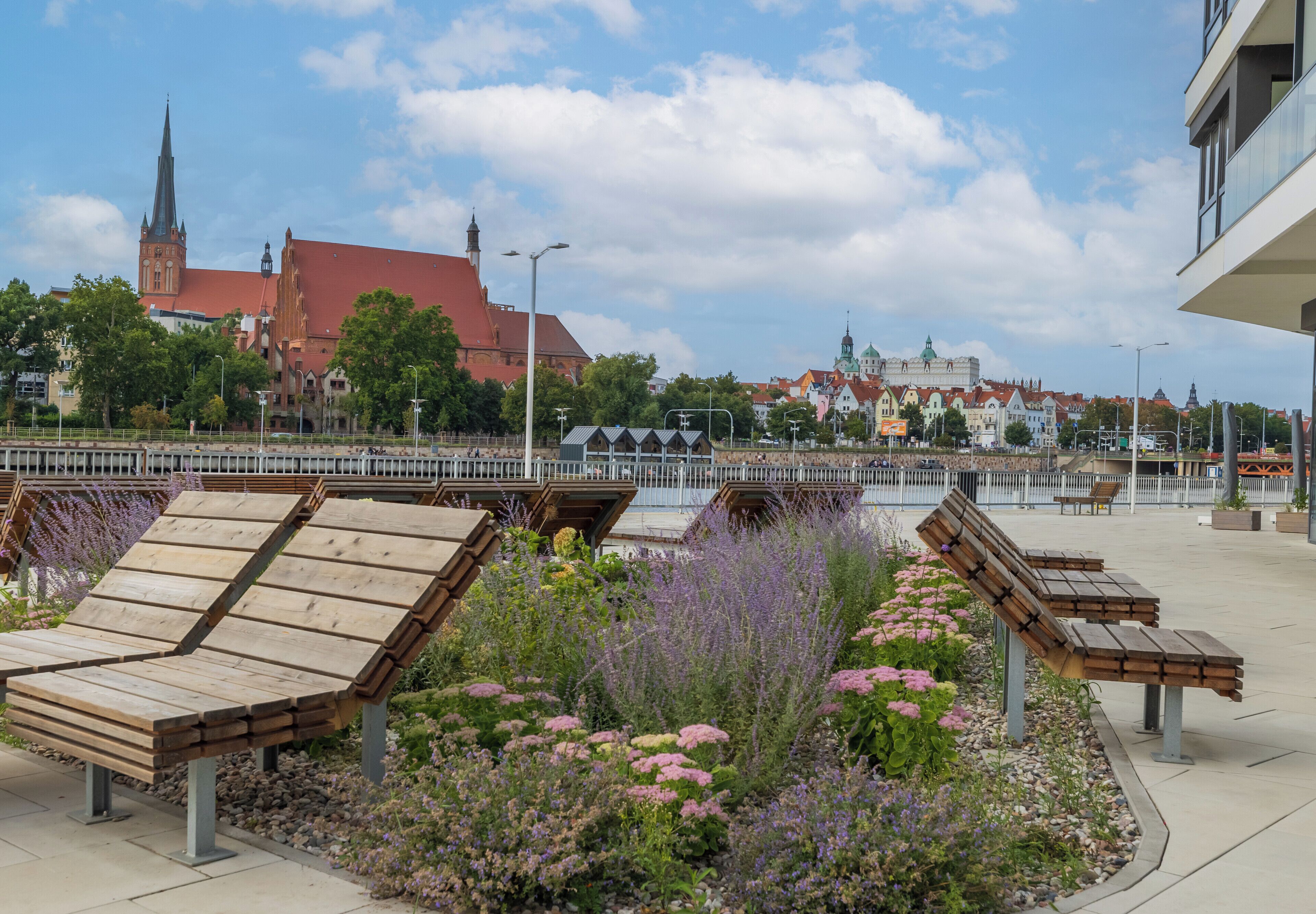 Eine Uferpromenade mit hölzernen Bänken und Blumenbeeten.