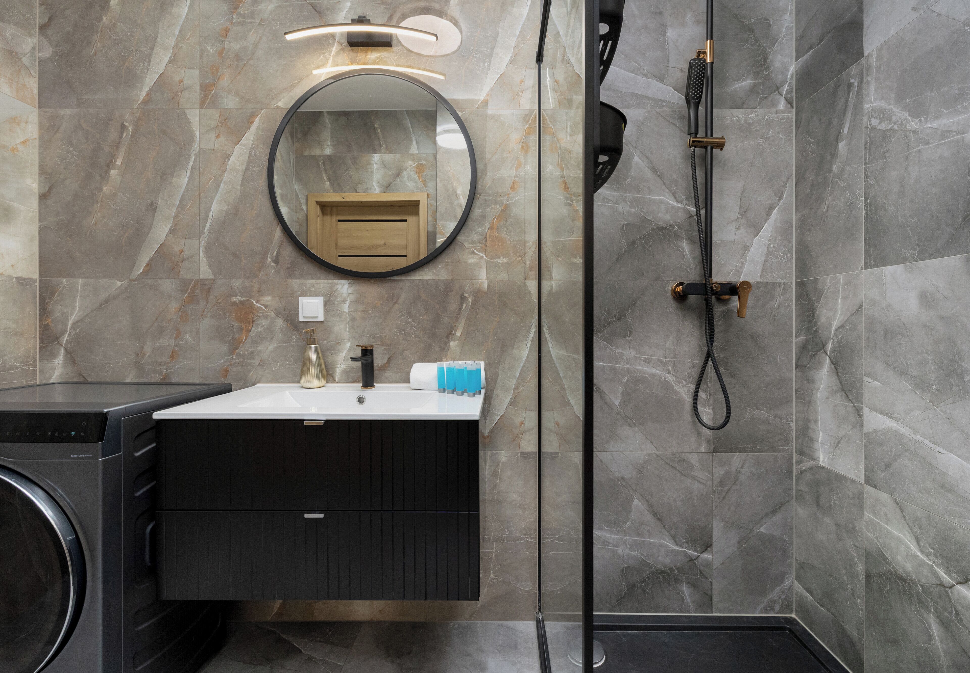 A bathroom with a round mirror, a sink, a shower, and a washing machine.