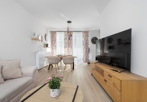 A modern living room with a sofa, a dining table with chairs, a TV, and a wooden cabinet. - Zielonego Mostu Cozy Elegant Apartment (Szczecin)
