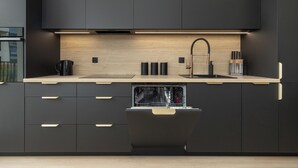 A modern kitchen with dark cabinetry, a wooden countertop, a built-in dishwasher, and a stainless steel sink. - Zielonego Mostu Cozy Elegant Apartment (Szczecin)
