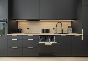A modern kitchen with dark cabinetry, a wooden countertop, a built-in dishwasher, and a stainless steel sink. - Zielonego Mostu Cozy Elegant Apartment (Szczecin)