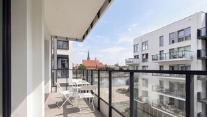 A balcony with a table and chairs, overlooking a cityscape with modern buildings and a church spire. - Zielonego Mostu Cozy Elegant Apartment (Szczecin)