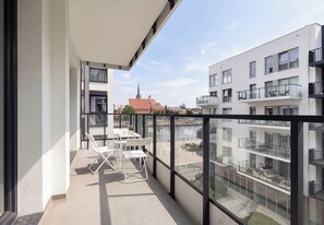 A balcony with a table and chairs, overlooking a cityscape with modern buildings and a church spire. - Zielonego Mostu Cozy Elegant Apartment (Szczecin)
