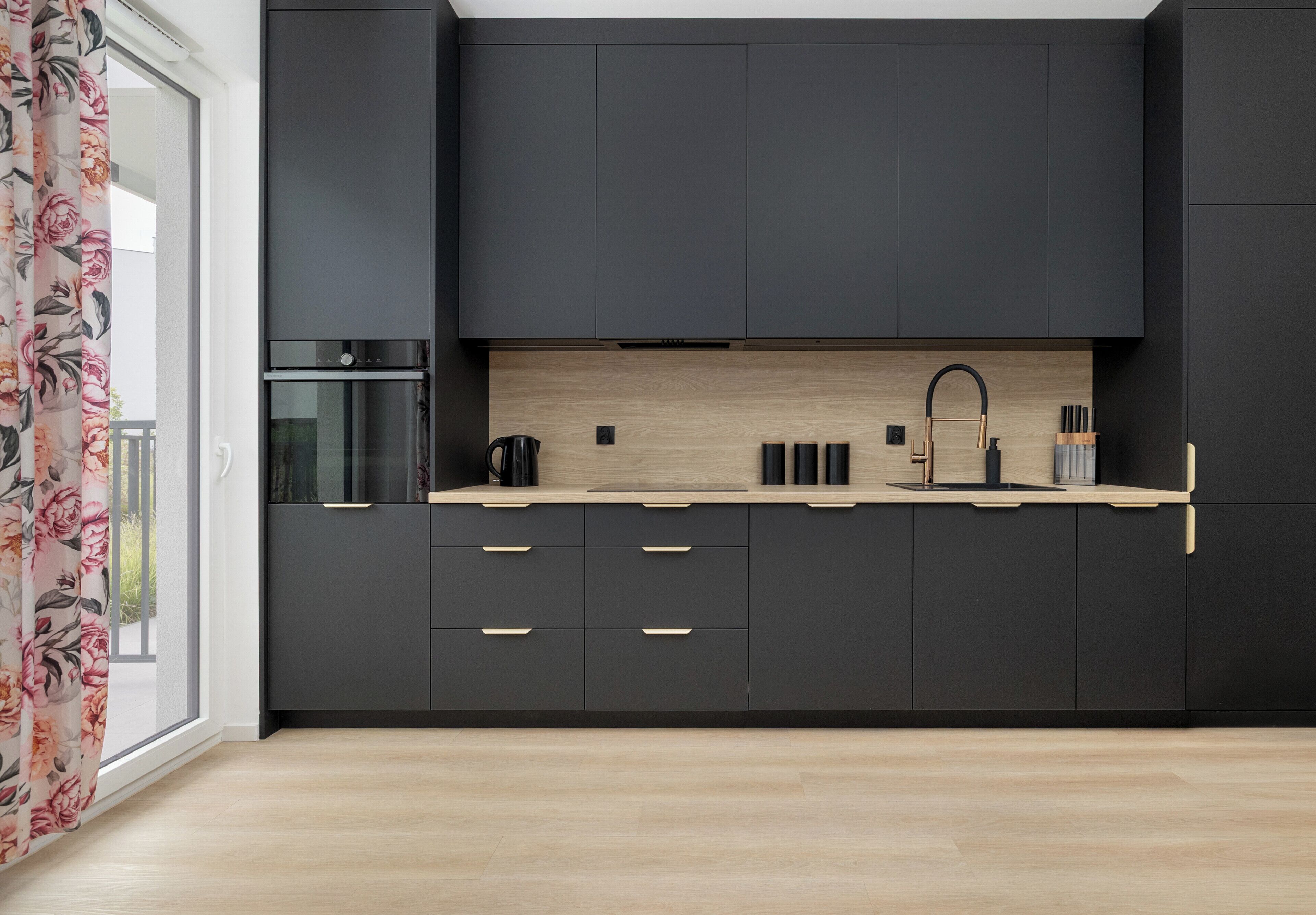 A modern kitchen with dark cabinetry, a wooden countertop, and a built-in oven.