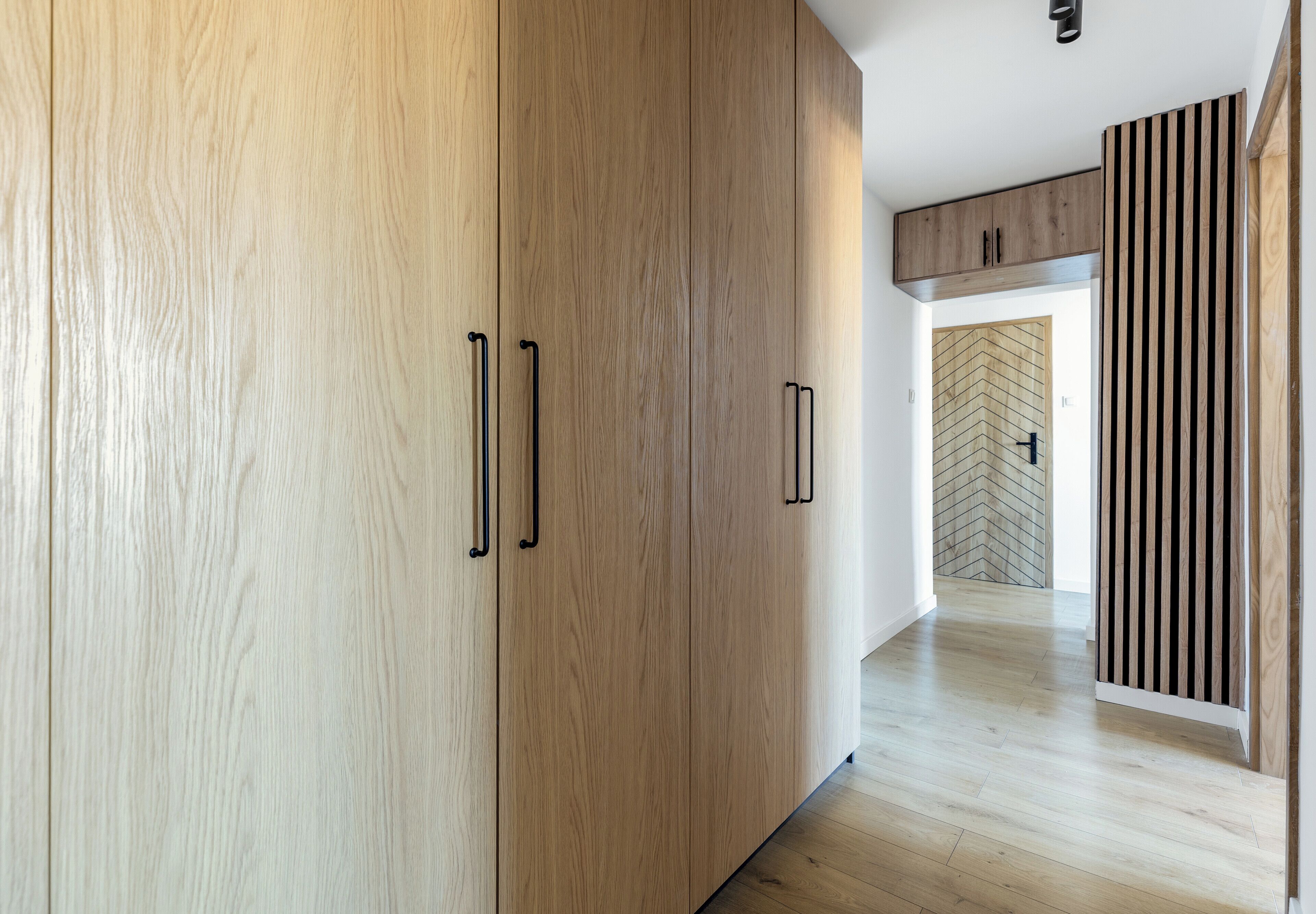Een gang met houten vloer en modern interieur, met een inloopkast en wandbekleding in herringbone patroon.