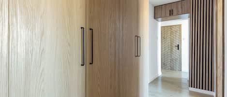A hallway with wooden flooring and a modern interior design, featuring a wardrobe with black handles and a herringbone-patterned wall.