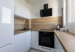 A compact kitchen with white cabinetry, a black dishwasher, a built-in oven, and a wooden countertop. - Asnyka Navy Wood Apartment (Szczecin)