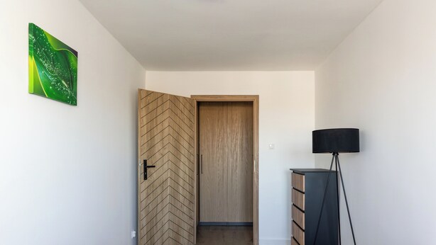 Un dormitorio con dos camas de madera, un armario de madera, una lámpara de pie y un cuadro abstracto verde en la pared.