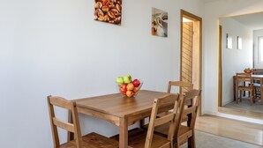 Un comedor con una mesa y sillas de madera, un frutero sobre la mesa y dos cuadros en la pared.