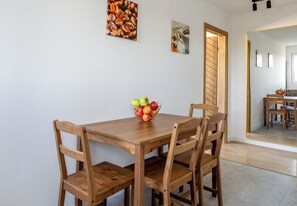 Ein Essbereich mit Holztisch und Stühlen, eine Obstschale auf dem Tisch sowie zwei Bilder an der Wand.