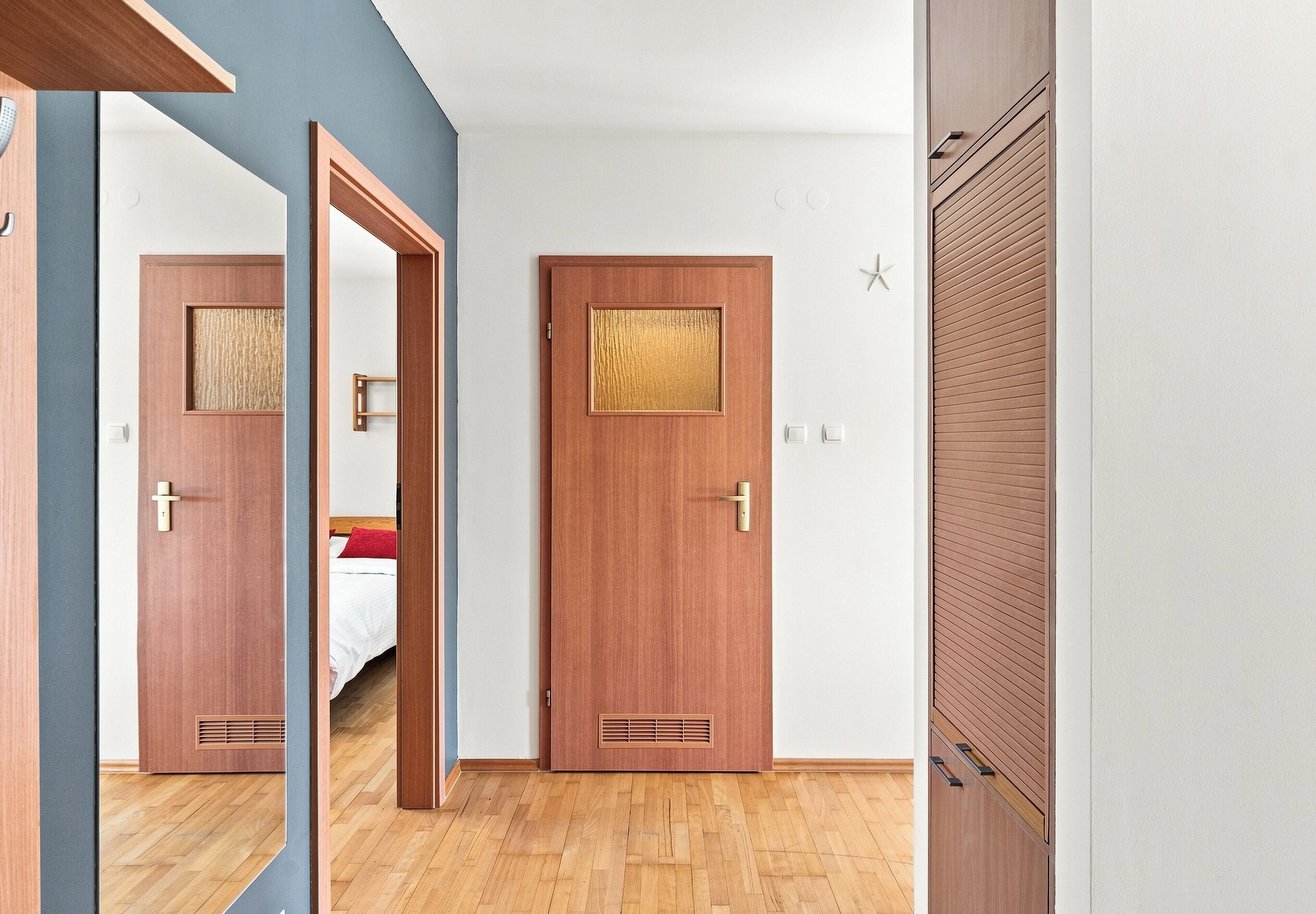 Une chambre d’hôtel avec une porte en bois, un lit avec une literie blanche, un oreiller rouge et une décoration en forme d’étoile de mer sur le mur.
