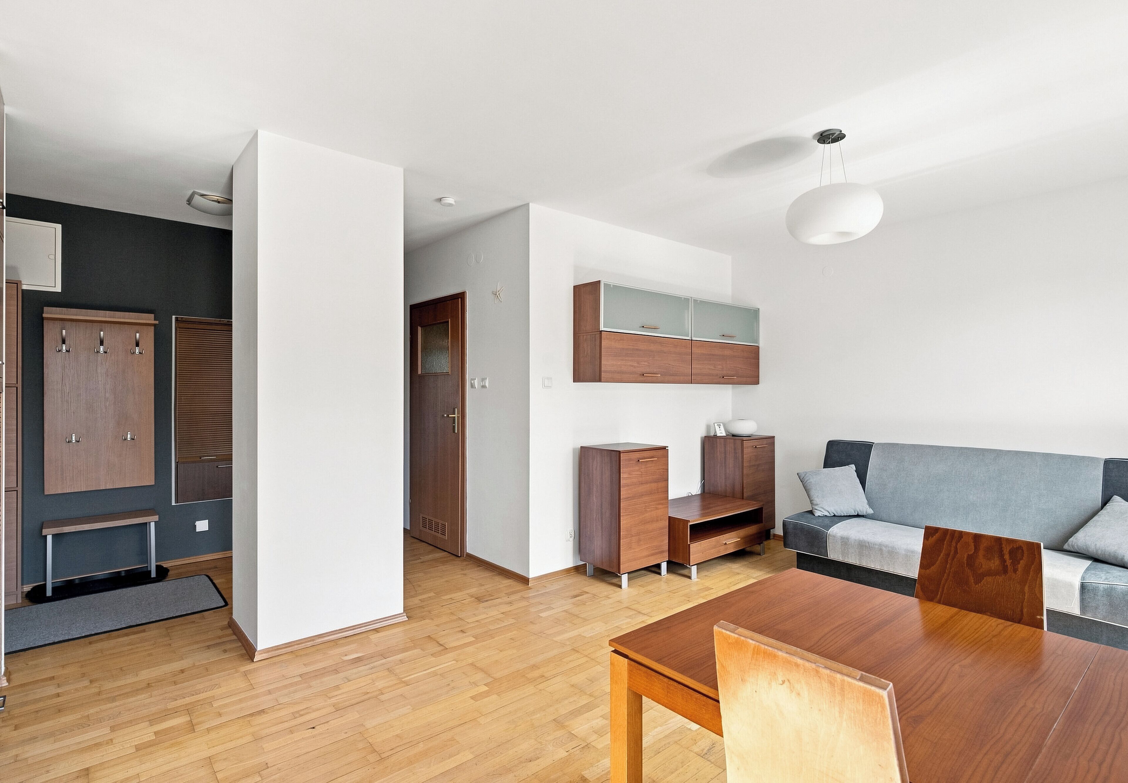 A modern living space with a dining area, built-in wooden cabinets, a grey sofa, and a ceiling light fixture.